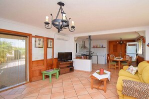 A living room with a television, a sofa, a dining area with chairs, and a kitchen in the background. - Cabin in Muro with swimming pool (Muro)