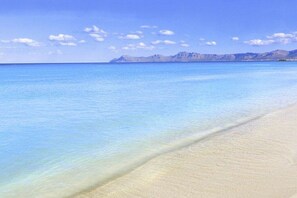 A beach with clear water and a distant mountain range.
