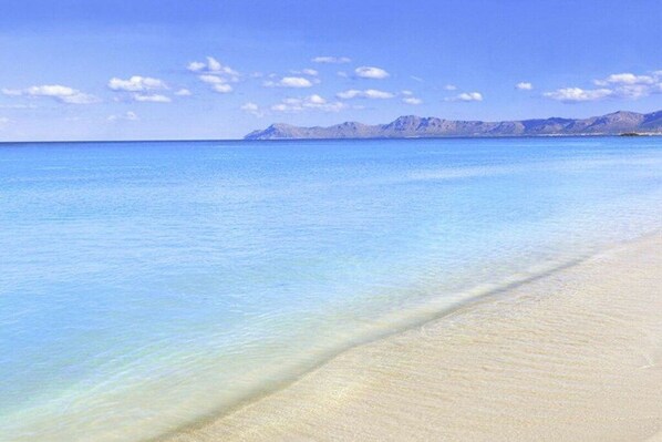 A beach with clear water and a distant mountain range.