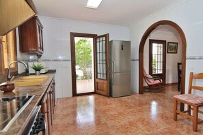 Eine Küche mit einem Edelstahl-Kühlschrank, einer Spüle und einem Herd. Ein Stuhl und eine Tür führen in einen Außenbereich.