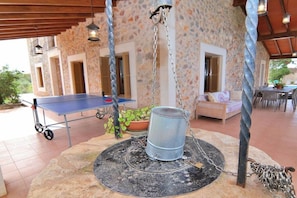 A covered outdoor area with a ping pong table, a metal barrel, and a seating area with cushions.
