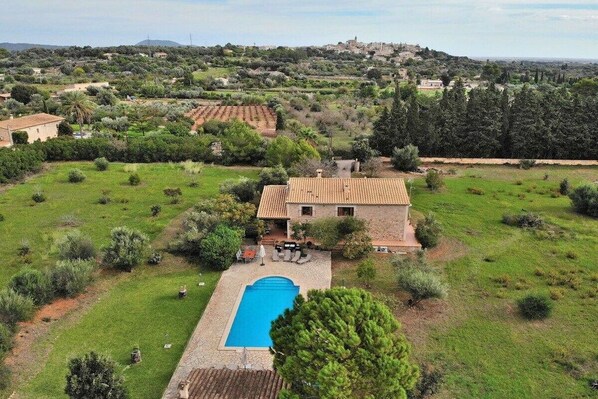 A villa with a swimming pool, surrounded by a lush garden and a hilly landscape in the background.