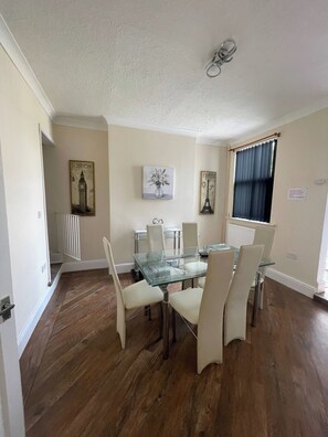A dining area with a glass table and chairs, a radiator, and wall art depicting landmarks. - The Cosy Nest - Overseal (Swadlincote)