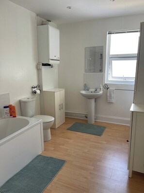 A bathroom with a toilet, sink, bathtub, and a window. - The Cosy Nest - Overseal (Swadlincote)