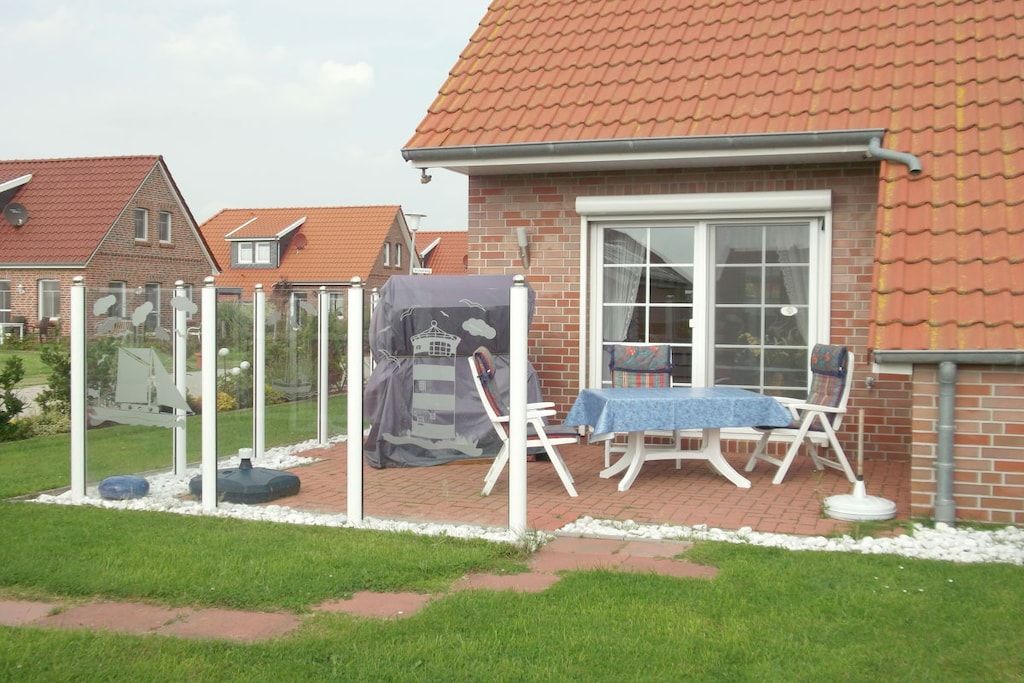 A residential property with a brick house, a covered outdoor seating area with a table and chairs, and a garden.