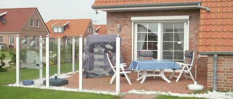 A residential property with a brick house, a covered outdoor seating area with a table and chairs, and a garden.