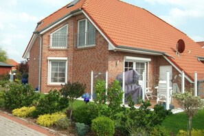A two-story house with a red-tiled roof, a brick exterior, and a front porch with white chairs. - Holiday home with 2 bedrooms (Krummhörn Greetsiel)