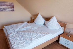 Ein ordentlich bezogenes Bett mit weißer Bettdecke und Kissen, einer Nachttischlampe und einer kleinen Kommode.