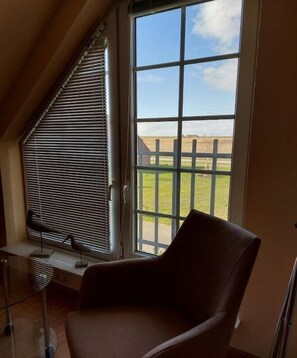 Ein Zimmer mit großem Fenster, einem Sessel und einem Schreibtisch mit Lampe.