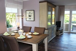 A dining area with a wooden table set for tea, a cabinet with drawers, and a television in the background. - Holiday home with 2 bedrooms (Greetsiel)