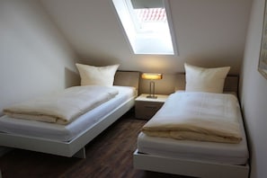 A bedroom with two beds, a skylight, and a bedside table with a lamp. - Holiday home with 2 bedrooms (Greetsiel)