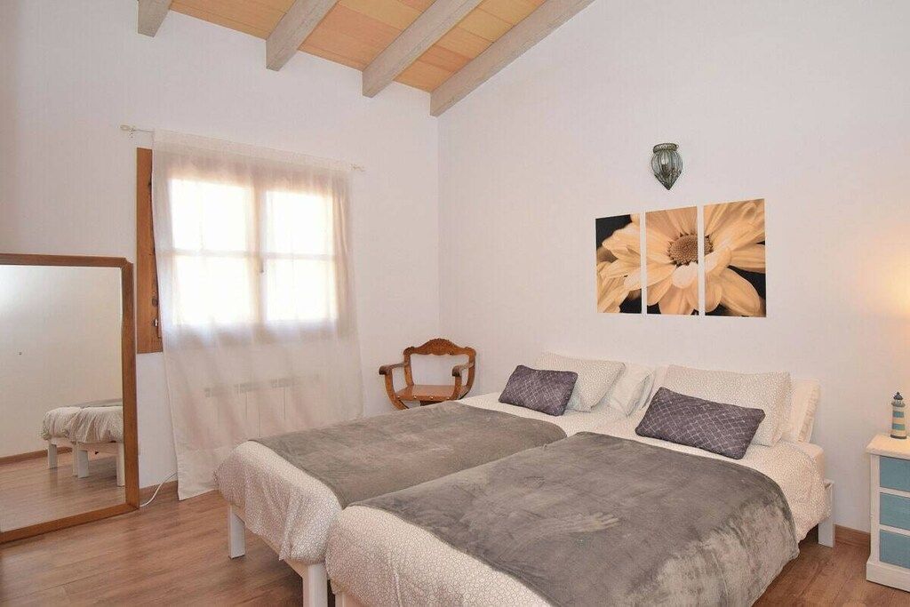 Un dormitorio con dos camas, una silla de madera, un espejo y una lámpara de pared.