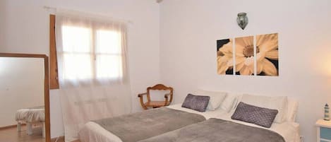 A bedroom with two beds, a wooden chair, a mirror, and a wall-mounted light fixture.