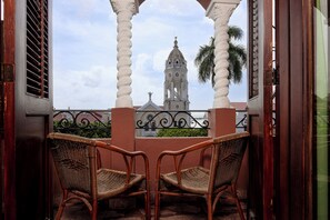 Un balcon avec deux fauteuils en osier, une vue sur un clocher et un palmier.