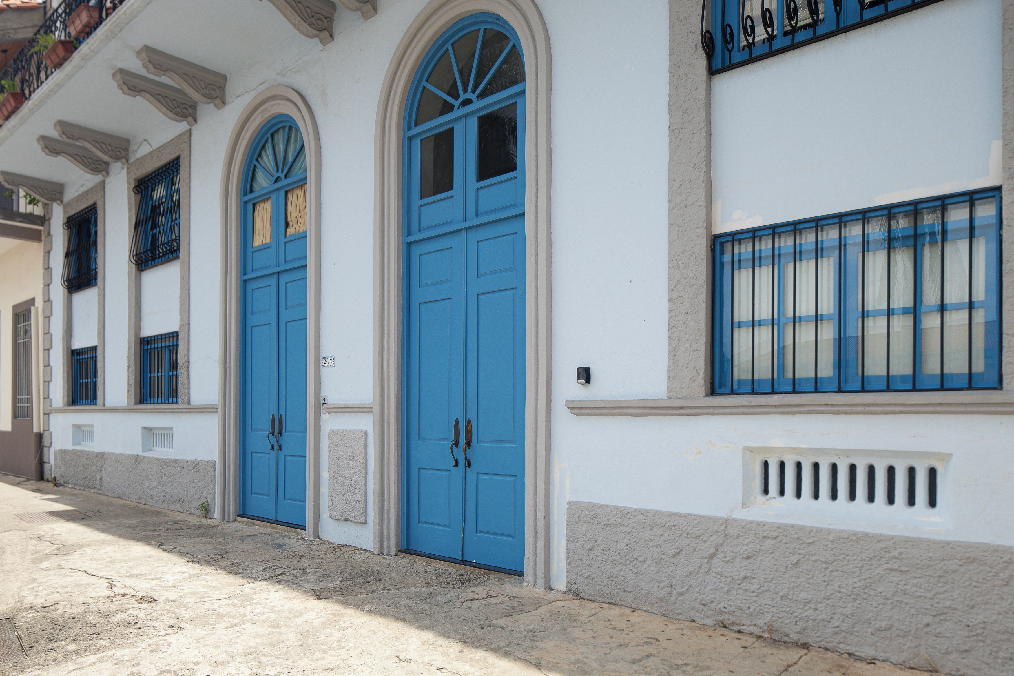 A building with three blue doors, a white facade, and a balcony with black railings.