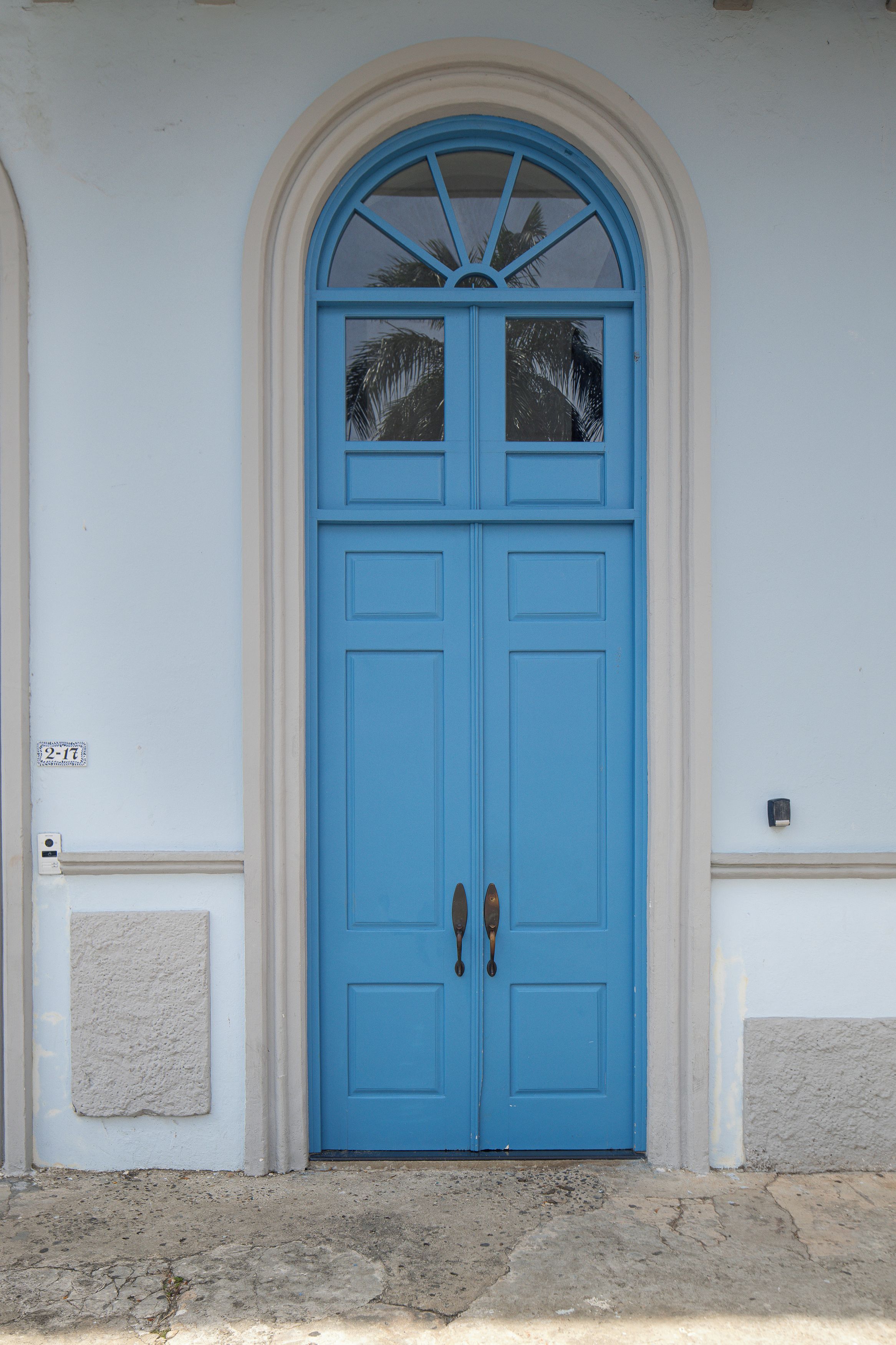 A blue double door with a decorative arch above it, set in a building with a plain facade.