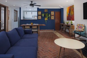 Un soggiorno con un divano blu, un tavolo da pranzo con sedie, un piccolo tavolino rotondo e una ventola a soffitto.