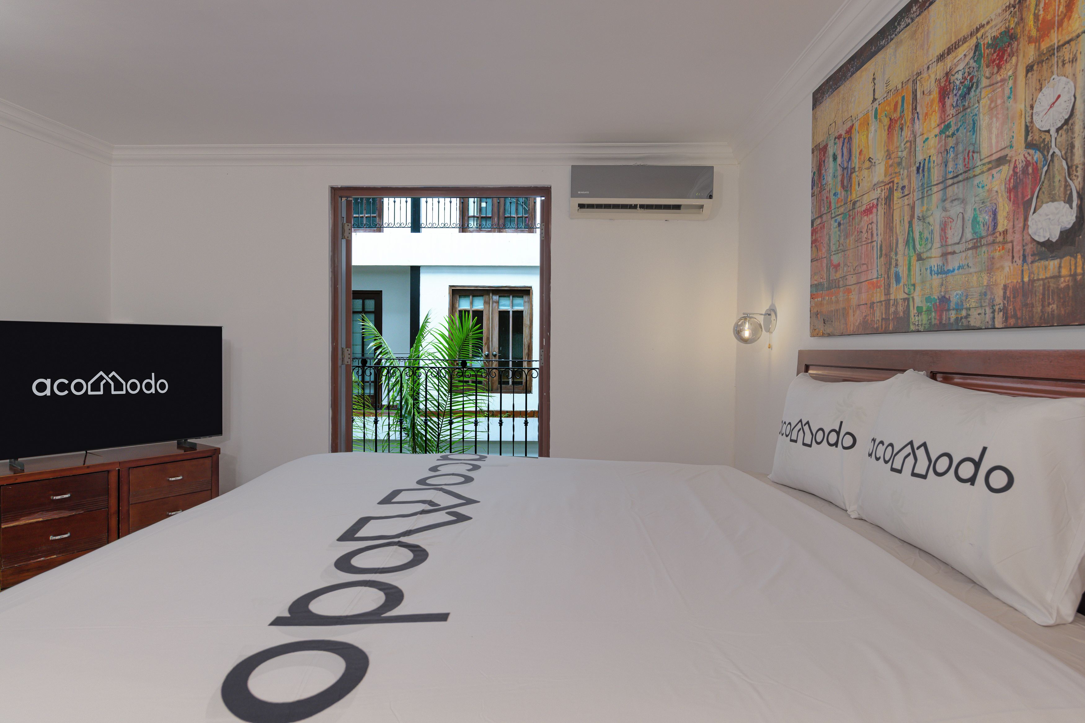 A hotel room with a bed, a television, a painting, and a view of the outside.