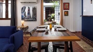 A dining area with a wooden table set for four, surrounded by chairs, a blue sofa, and a small side table with a lamp.