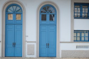 Two blue doors with arched windows, a white wall, and a window with a metal grill. - 2 Hab. + 1.5 Baños | Dúplex de dos niveles con balcón | Casco Viejo | Estadías de 30+ noches (Casco Viejo)