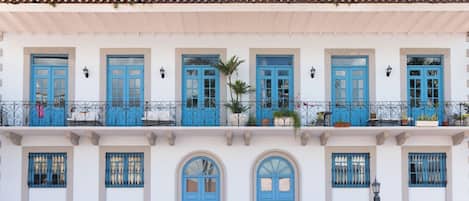 A building with multiple balconies, blue doors, and windows with metal grilles.