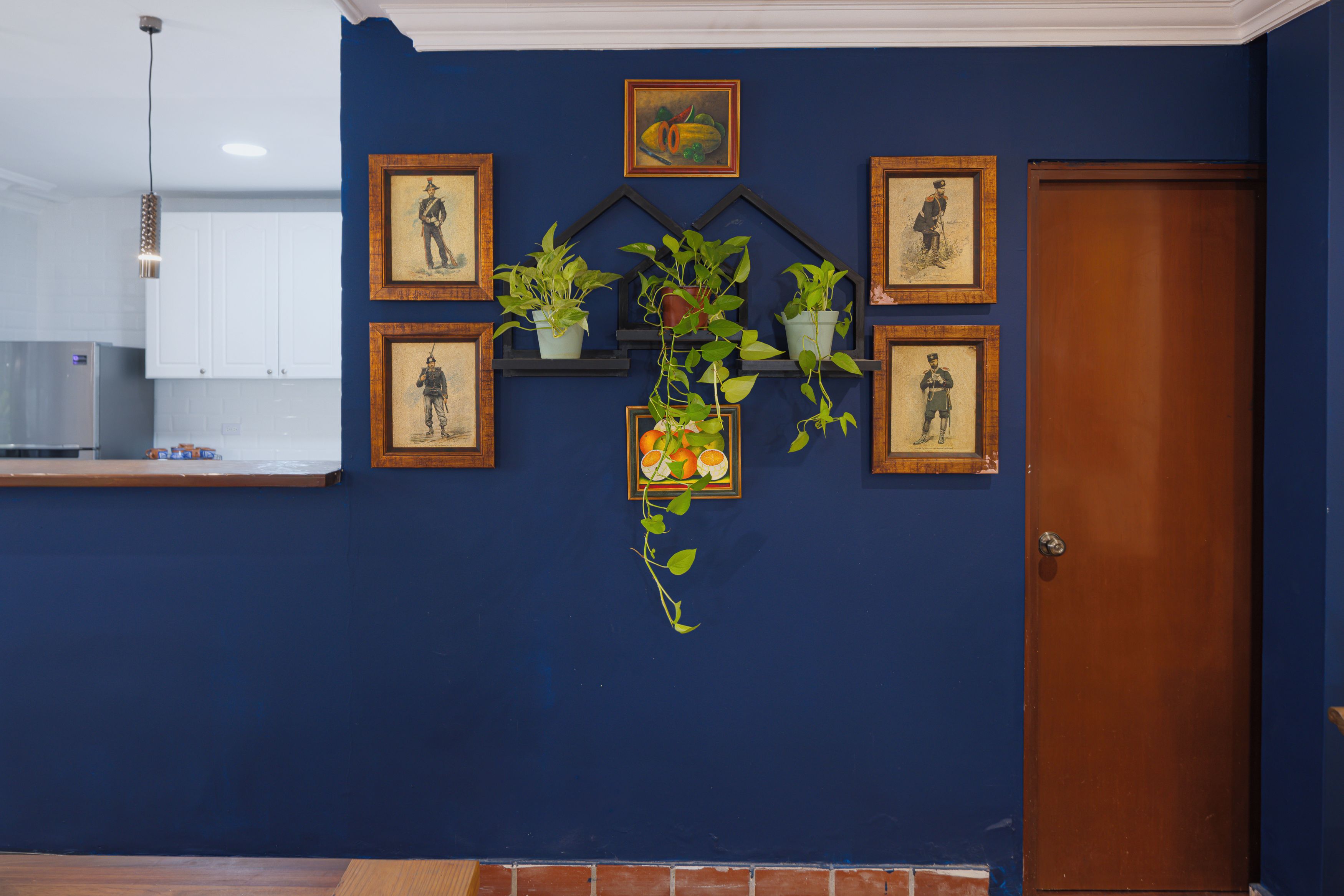 A room with a blue wall, a wooden door, and a kitchen area with a white cabinet and a hanging light fixture.