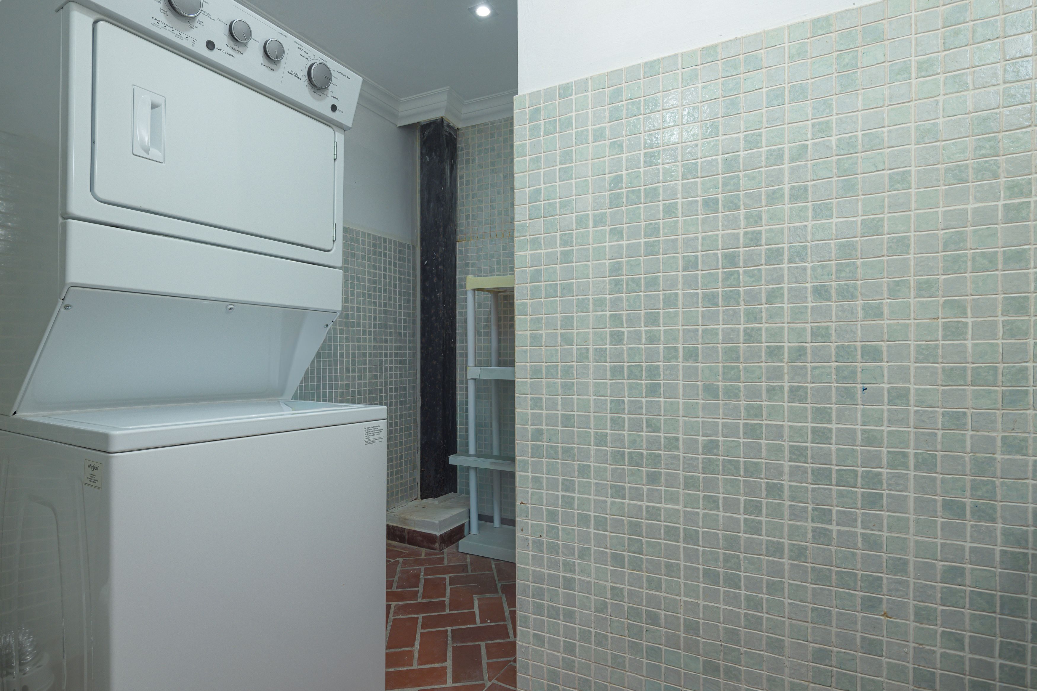 A compact kitchen with a built-in washer and dryer, a tiled backsplash, and a brick-patterned floor.