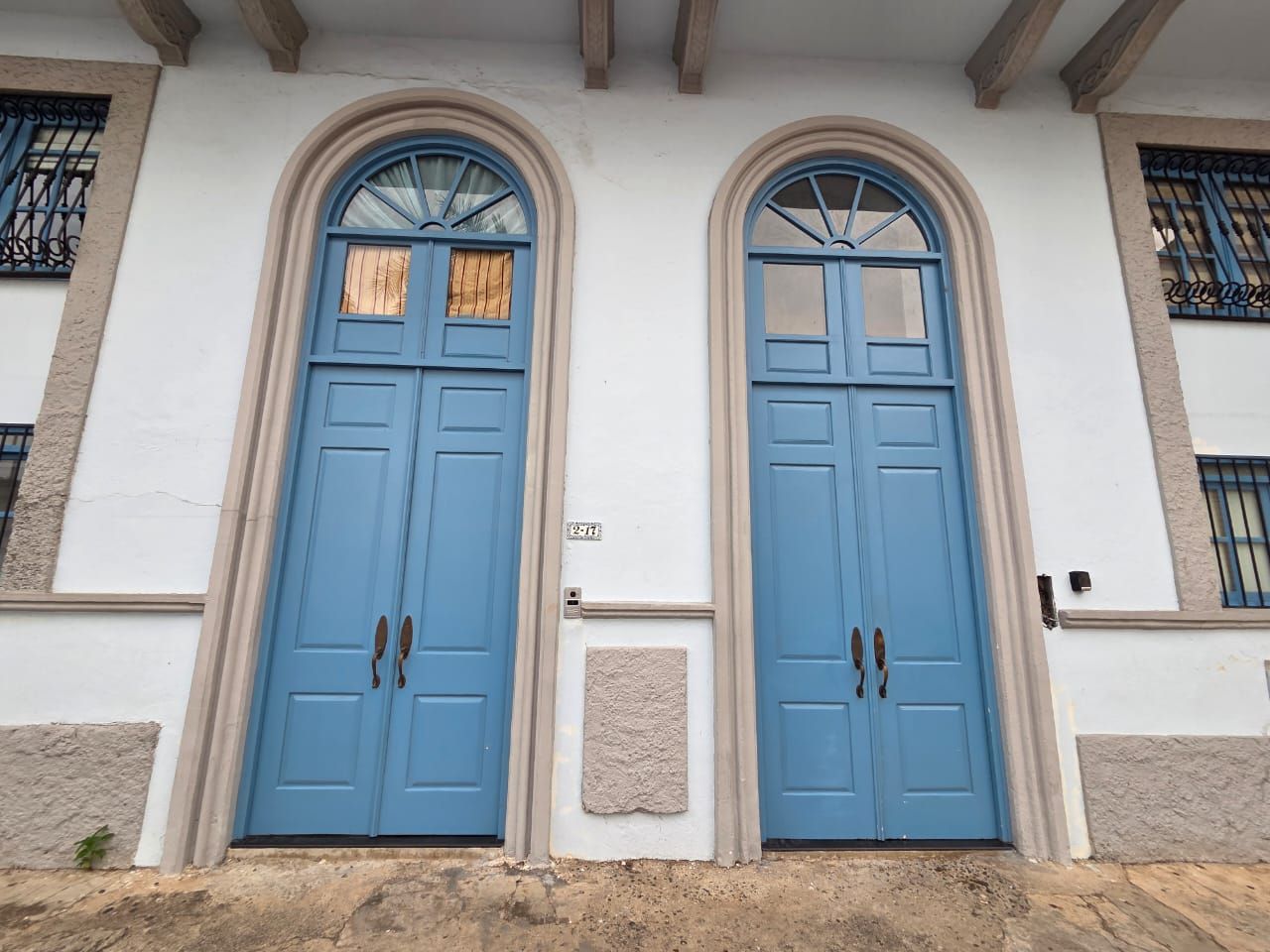 A building with two blue doors, a small plaque, and a window with a barred design.