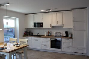A modern kitchen with white cabinets, a microwave, an oven, and a coffee maker. - Holiday apartment with 2 bedrooms (Krummhörn-Greetsiel)