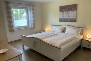 A bedroom with a bed, bedside tables, a window with curtains, and a painting on the wall. - Holiday apartment with 2 bedrooms (Krummhörn-Greetsiel)
