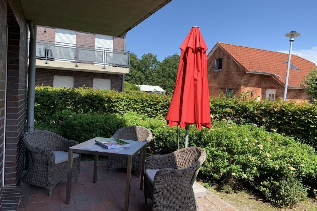 An outdoor patio with wicker furniture, a table, and a red umbrella.