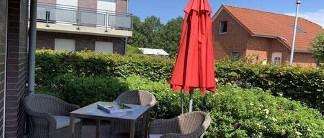 An outdoor patio with wicker furniture, a table, and a red umbrella.