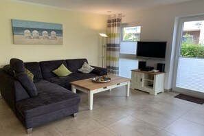 A living room with a dark sofa, a wooden coffee table, a television on a stand, and a painting on the wall. - Holiday apartment with 2 bedrooms (Krummhörn-Greetsiel)