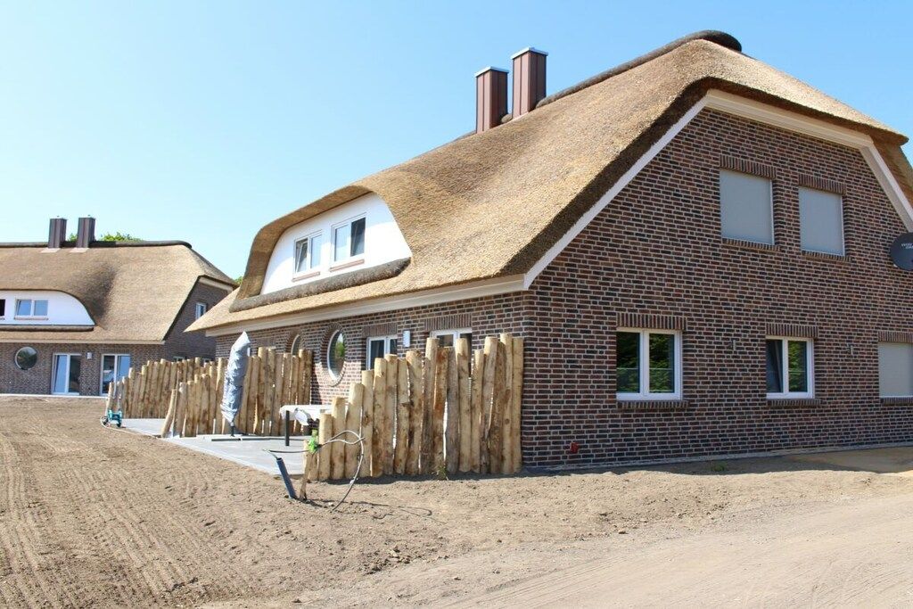 A brick house with a thatched roof and a wooden fence.