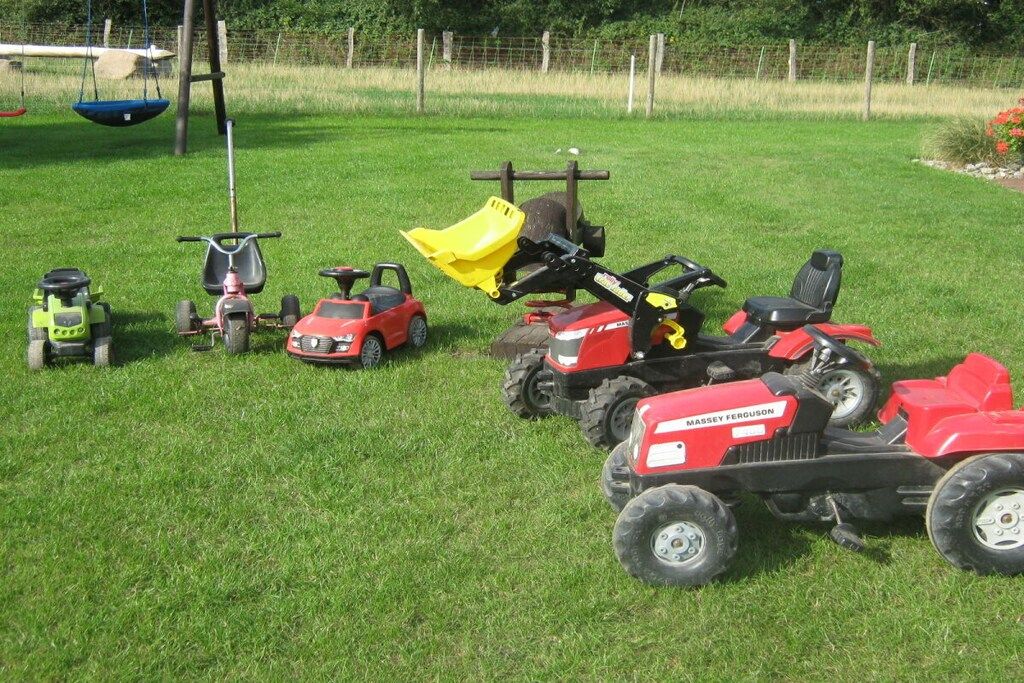 Een gazon met verschillende speelvoertuigen, waaronder een rode tractor en een groene tractor.