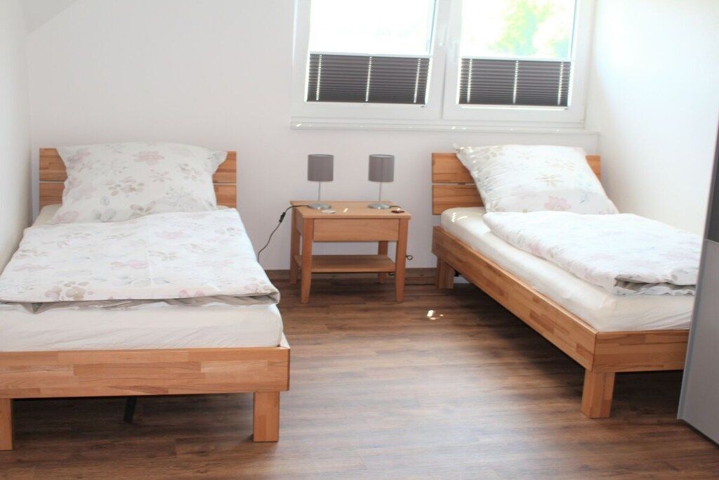 A bedroom with two wooden beds, a nightstand with lamps, and a window with blinds.