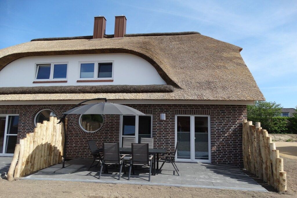 Een huis met rieten dak, bakstenen gevel en een terras met tuinmeubilair.