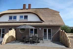 Ein Haus mit Strohdach, Backsteinfassade und einer Terrasse mit Gartenmöbeln.