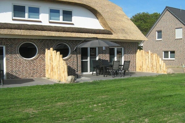 Ein Haus mit einem Strohdach, Ziegelwänden und einer Terrasse mit Gartenmöbeln.