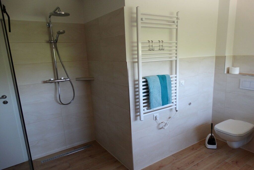 A bathroom with a shower, a towel rack, a toilet, and a floor vent.