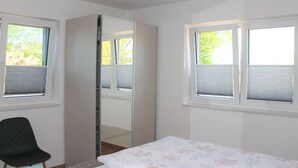 A bedroom with a bed, a chair, a wardrobe, and two windows with blinds. - Farm in Dahme with sauna and Wi-Fi (Dahme)