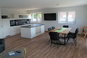 A modern kitchen with white cabinetry, a central island, and a dining area with a wooden table and chairs.