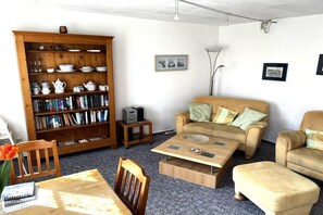 A living room with a sofa, coffee table, bookshelf, and a lamp. - Holiday apartment with 1 bedroom (Schönberg)