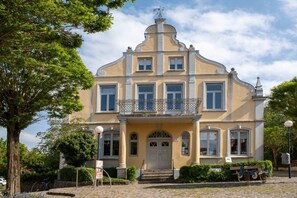 A two-story building with a balcony, a central entrance with steps, and a symmetrical facade. - Holiday apartment with 1 bedroom (Schönberg)