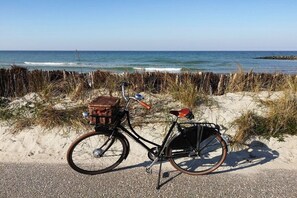 Un vélo est garé sur une plage de sable, avec un panier et une selle, et offre une vue sur l’océan.