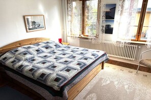Une chambre à coucher avec un lit en bois, une courtepointe, un radiateur, des rideaux en dentelle et un tableau encadré accroché au mur.