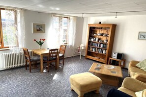 A cozy living room with a wooden table, chairs, a bookshelf, and a sofa. - Holiday apartment with 1 bedroom (Schönberg)