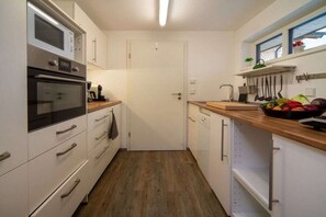 A compact kitchen with white cabinets, a microwave, an oven, and a wooden countertop. - Apartment in Bolsterlang with swimming pool (Bolsterlang)