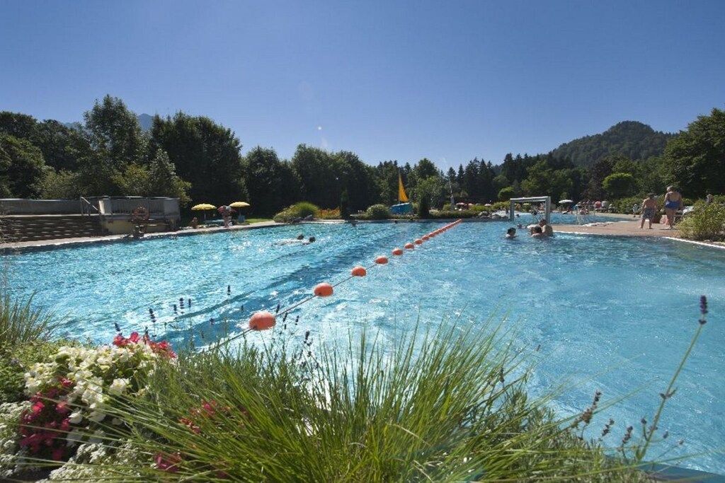 A swimming pool with multiple lanes, surrounded by greenery and a mountainous backdrop.
