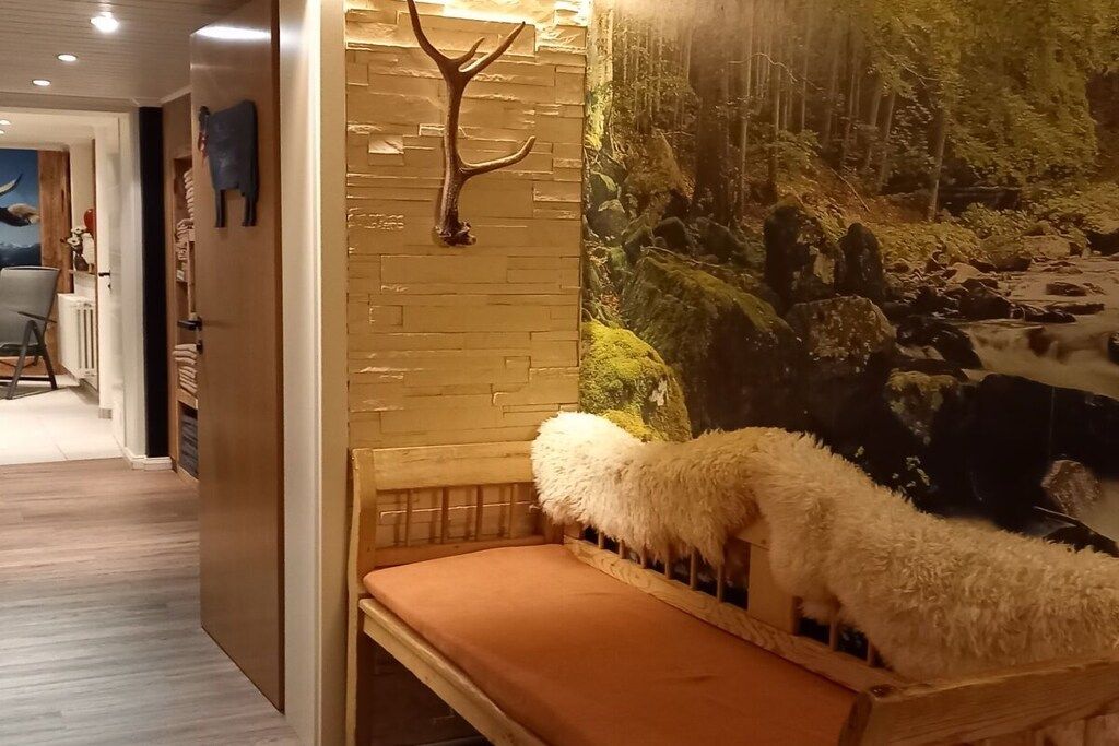 Quarto com um banco de madeira, cabeça de veado fixada na parede e um mural com uma cena de floresta.